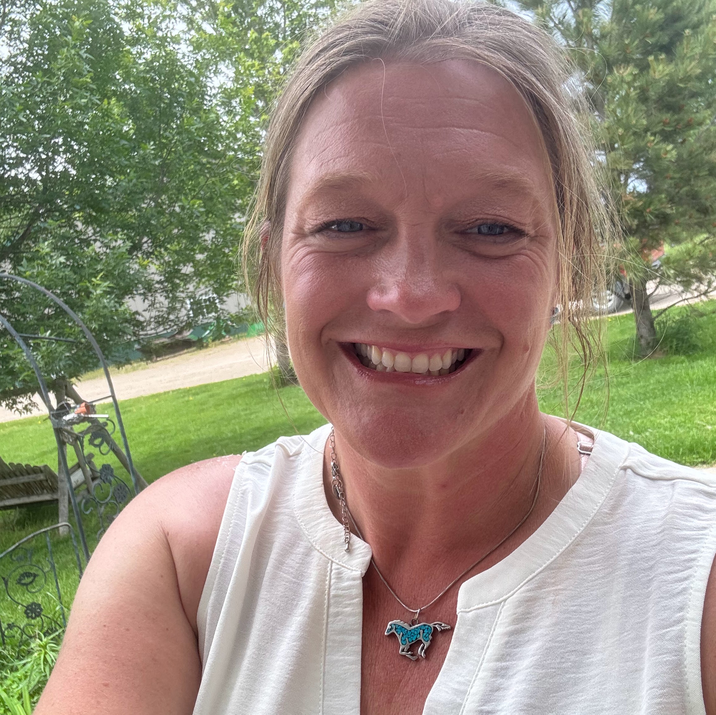 Selfie of a woman in white shirt, horse necklace, and earthy presence in the out doors.